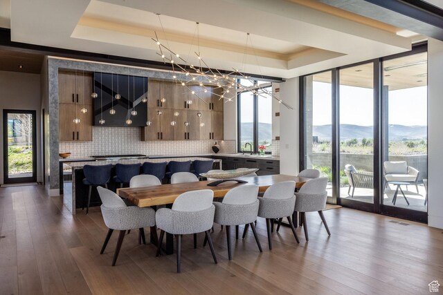 7744 E Moon Dance Cir, Kamas, UT 84036 - dining space with a tray ceiling, wood finished floors, a chandelier, a wall of windows, and a mountain view