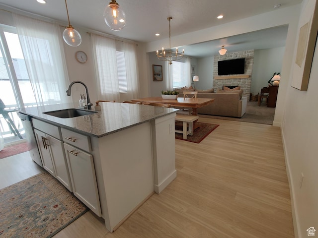 2132 N Elderberry Dr W, Saratoga Springs, UT 84045 - kitchen with a sink, a stone fireplace, light wood finished floors, a kitchen island with sink, and hanging light fixtures