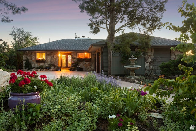 4774 S Oak Terrace Dr, Millcreek, UT 84124 - back of property at dusk with stone siding, a patio area, a shingled roof, and french doors