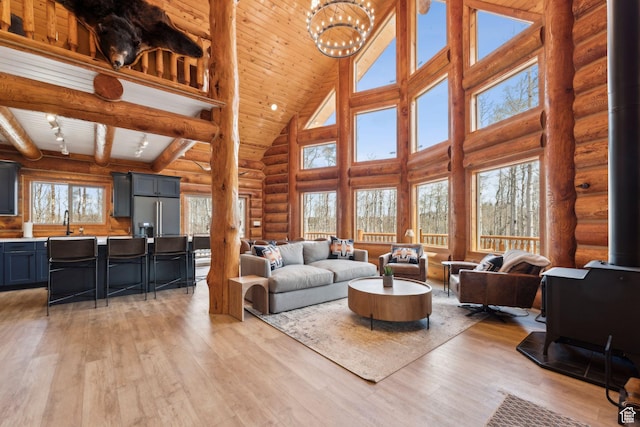 1085 Moose Hollow Rd, Robertson, WY 82944 - living room with high vaulted ceiling, a wood stove, rustic walls, light wood-style floors, and a chandelier