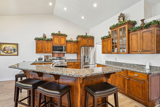 9451 S Peaceful View Way S, Jordan, UT 84095 - kitchen with stainless steel appliances, light wood-style floors, glass insert cabinets, a breakfast bar, and high vaulted ceiling