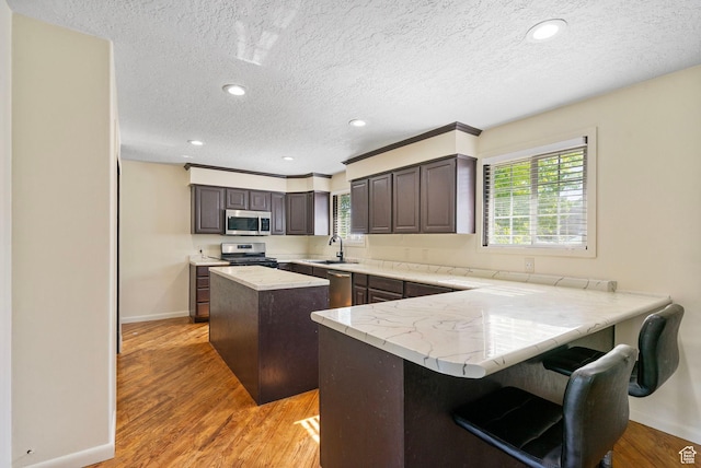 4589 S Trojan Dr, West Valley City, UT 84120 - kitchen with appliances with stainless steel finishes, a center island, baseboards, light wood-type flooring, and a textured ceiling