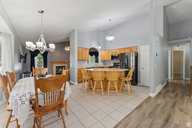 192 Starboard Ln, Stansbury Park, UT 84074 - dining room with a chandelier, high vaulted ceiling, baseboards, light wood-style flooring, and a fireplace