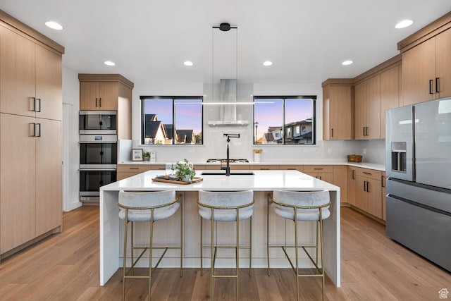 12719 S Outlaw Pl E, Draper, UT 84020 - kitchen featuring appliances with stainless steel finishes, wall chimney range hood, light wood-type flooring, light countertops, and a kitchen breakfast bar