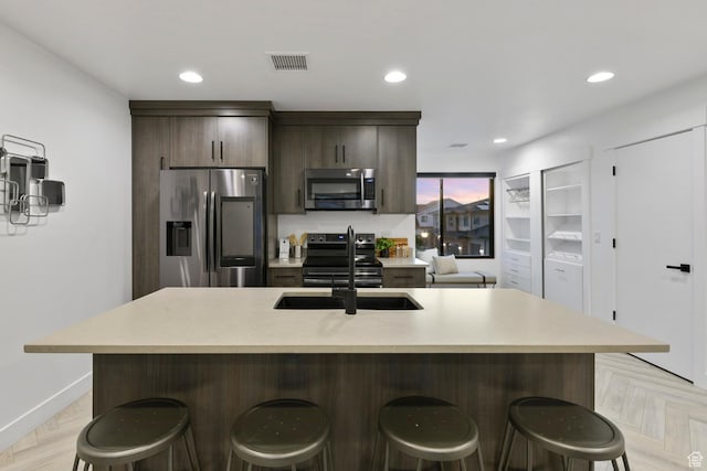 12719 S Outlaw Pl E, Draper, UT 84020 - kitchen featuring stainless steel appliances, a breakfast bar, light countertops, an island with sink, and dark brown cabinetry