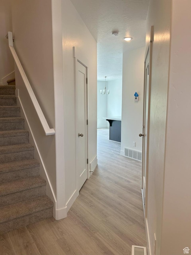 5118 E Lakefield Dr N, Eagle Mountain, UT 84005 - hall featuring stairs, light wood-type flooring, a chandelier, baseboards, and a textured ceiling