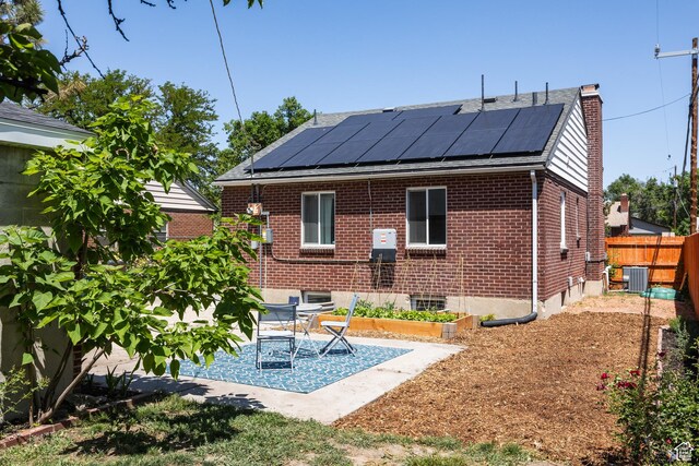 1217 Talisman Dr, Salt Lake City, UT 84116 - back of property with cooling unit, roof mounted solar panels, a chimney, brick siding, and a patio area