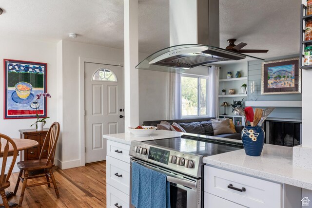 1217 Talisman Dr, Salt Lake City, UT 84116 - kitchen with stainless steel range with electric stovetop, island range hood, light wood finished floors, ceiling fan, and white cabinetry
