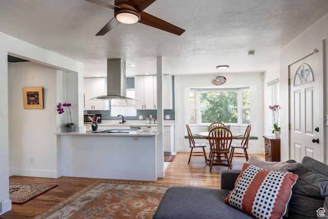 1217 Talisman Dr, Salt Lake City, UT 84116 - kitchen featuring island exhaust hood, ceiling fan, white cabinets, decorative backsplash, and light wood-style floors
