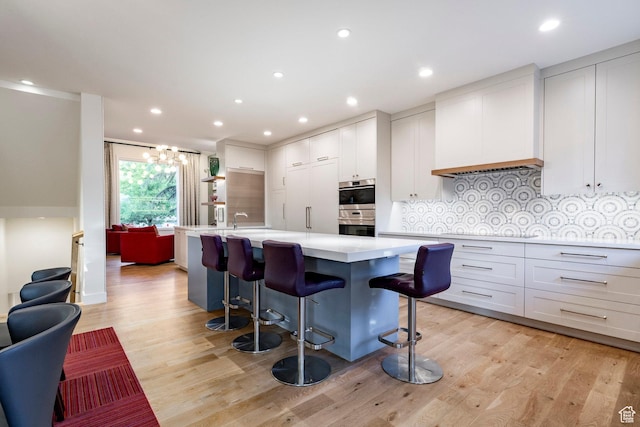 5972 S Ragsdale Dr, Murray, UT 84121 - kitchen featuring stainless steel double oven, light countertops, light wood-type flooring, backsplash, and an island with sink