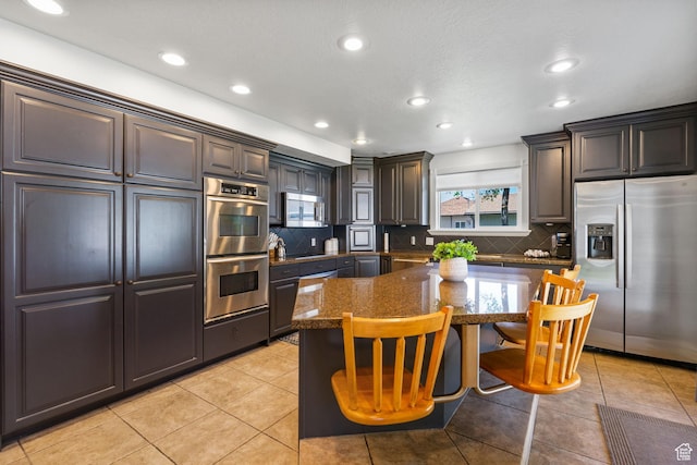 993 E 12600 S, Draper, UT 84020 - kitchen featuring appliances with stainless steel finishes, decorative backsplash, a kitchen bar, light tile patterned flooring, and a center island
