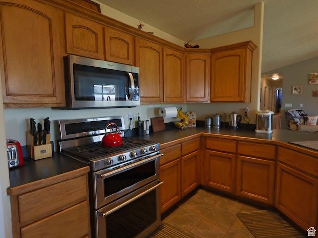 113 N 4950 W, West Point, UT 84015 - kitchen featuring stainless steel appliances, vaulted ceiling, dark countertops, and brown cabinets