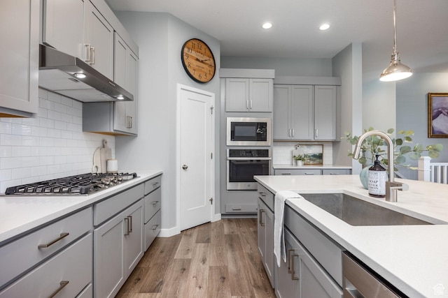 5067 W Beach Comber Way S, South Jordan, UT 84009 - kitchen featuring appliances with stainless steel finishes, gray cabinets, under cabinet range hood, a sink, and backsplash
