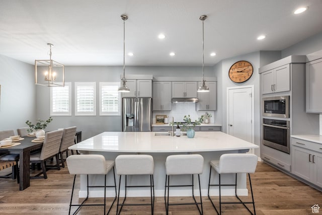 5067 W Beach Comber Way S, South Jordan, UT 84009 - kitchen with appliances with stainless steel finishes, gray cabinetry, under cabinet range hood, a kitchen breakfast bar, and recessed lighting