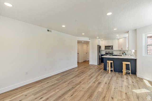 116 E Resaca Unit F3, Midvale, UT 84070 - kitchen with stainless steel appliances, recessed lighting, a kitchen bar, light wood-type flooring, and white cabinets