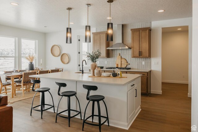 3537 E 1120 S Unit 110, Spanish Fork, UT 84660 - kitchen featuring wall chimney exhaust hood, a kitchen breakfast bar, decorative backsplash, light countertops, and a kitchen island with sink