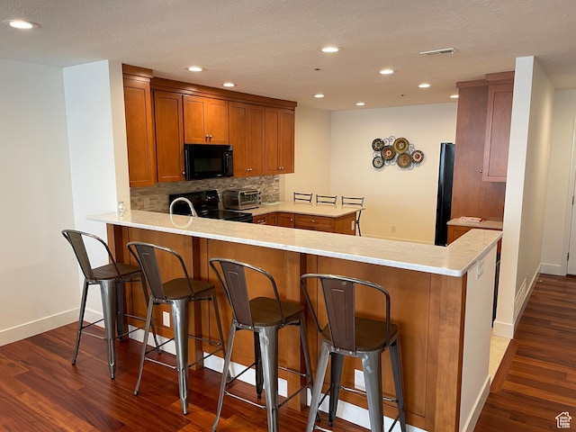 44 W 300 S Unit 1107N, Salt Lake City, UT 84101 - kitchen with black appliances, a peninsula, brown cabinets, dark wood-type flooring, and backsplash