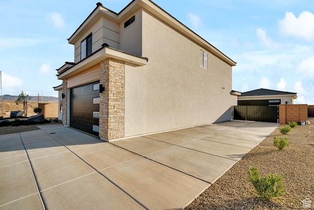 6068 S White Trails Dr, St George, UT 84790 - view of side of property with stone siding, stucco siding, an attached garage, concrete driveway, and a gate