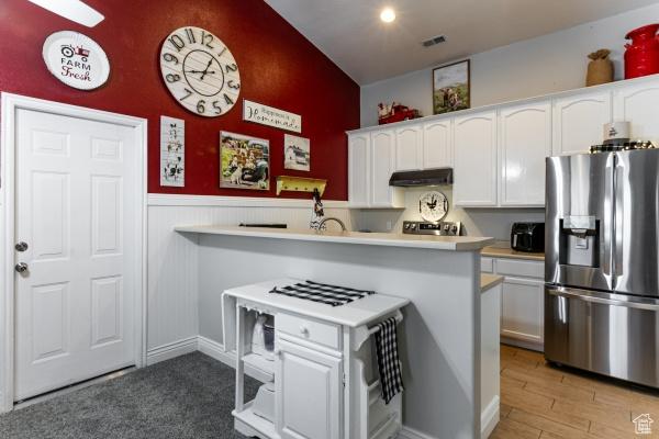 4732 W Wagon Train Dr, Herriman, UT 84096 - kitchen with stainless steel fridge, under cabinet range hood, white cabinets, light countertops, and a wainscoted wall