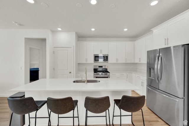 7405 W Glowing Sky Dr S, West Valley City, UT 84081 - kitchen featuring appliances with stainless steel finishes, a sink, light wood finished floors, a center island with sink, and white cabinetry