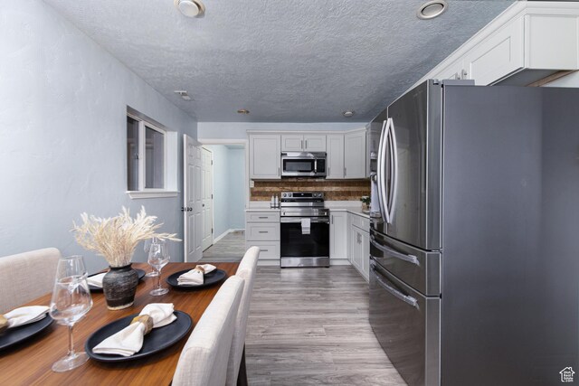 4815 W 4895 S, Kearns, UT 84118 - kitchen featuring stainless steel appliances, light wood-style flooring, backsplash, white cabinetry, and a textured ceiling