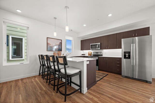 1034 W 1700 S Unit 121, Salt Lake City, UT 84104 - kitchen featuring appliances with stainless steel finishes, a breakfast bar, dark brown cabinetry, wood finished floors, and recessed lighting