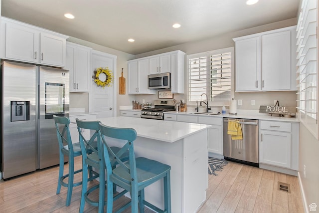1295 E Granite Peak Rd, Eagle Mountain, UT 84005 - kitchen with stainless steel appliances, a sink, white cabinetry, light wood finished floors, and a center island