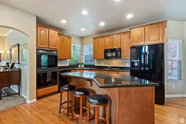 6512 S Timpanogos Way W, Taylorsville, UT 84129 - kitchen featuring black appliances, a center island, light wood-style flooring, arched walkways, and a breakfast bar area
