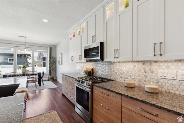 3222 W Harvard Dr, Mountain Green, UT 84050 - kitchen with appliances with stainless steel finishes, dark wood-type flooring, glass insert cabinets, decorative backsplash, and dark stone countertops