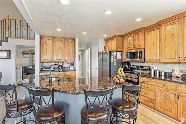 14263 S Morning Light Dr W, Herriman, UT 84065 - kitchen featuring appliances with stainless steel finishes, a sink, light wood-type flooring, a kitchen breakfast bar, and tasteful backsplash