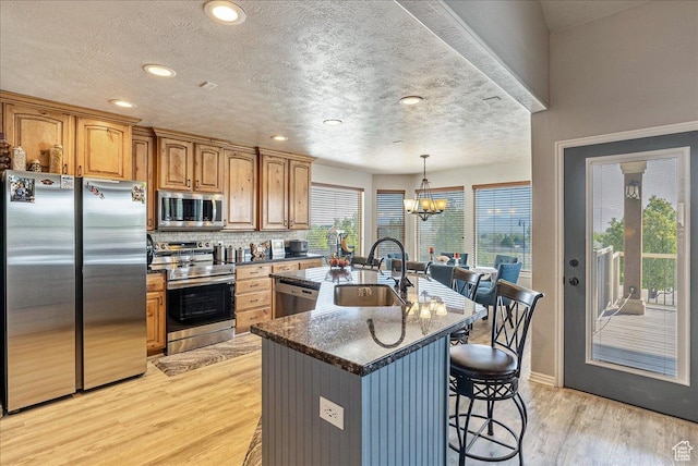 14263 S Morning Light Dr W, Herriman, UT 84065 - kitchen with appliances with stainless steel finishes, a sink, light wood-style floors, a kitchen breakfast bar, and a center island with sink