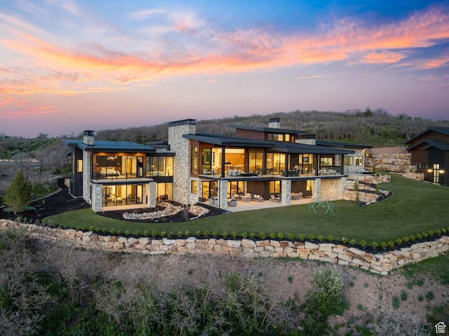 1735 Red Hawk Trl, Park City, UT 84098 - back of property at dusk featuring a patio area, a chimney, a balcony, a lawn, and stone siding