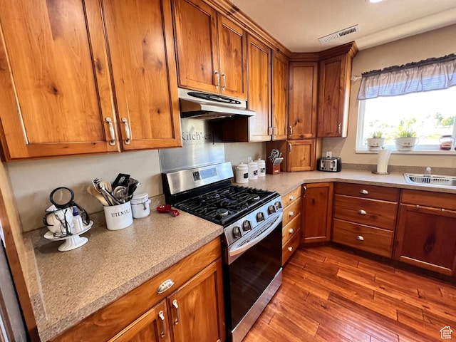 505 W 300 N, Orangeville, UT 84537 - kitchen with gas range, under cabinet range hood, brown cabinets, wood finished floors, and a sink