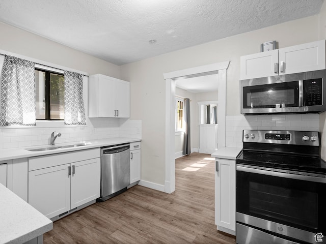 719 E 22nd St, Ogden, UT 84401 - kitchen with appliances with stainless steel finishes, a sink, backsplash, white cabinetry, and a textured ceiling
