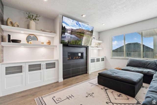 1006 W Firelock Way S, Bluffdale, UT 84065 - living room featuring a textured ceiling, light wood-style floors, a tiled fireplace, baseboards, and recessed lighting
