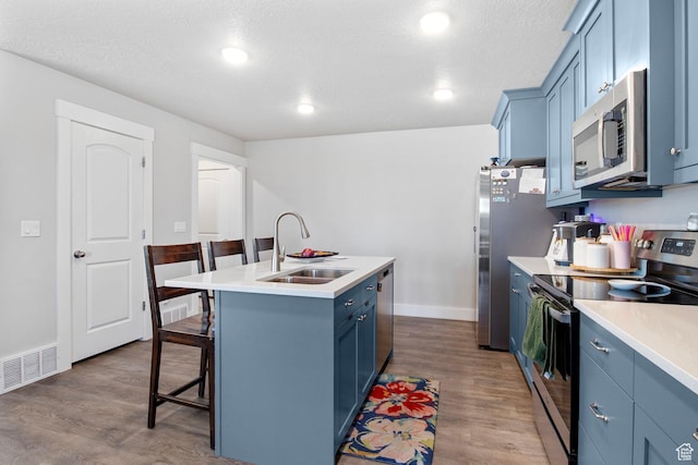 432 W 1470 N, Tooele, UT 84074 - kitchen with appliances with stainless steel finishes, blue cabinets, a breakfast bar area, a kitchen island with sink, and wood finished floors