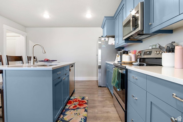 432 W 1470 N, Tooele, UT 84074 - kitchen with stainless steel appliances, blue cabinetry, light countertops, a center island with sink, and light wood-type flooring