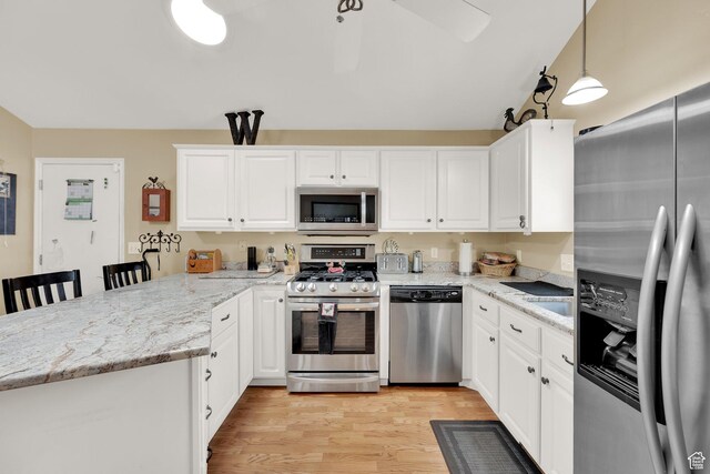 1127 W Monticello Ln, Murray, UT 84123 - kitchen with appliances with stainless steel finishes, a peninsula, white cabinetry, light wood finished floors, and light stone counters