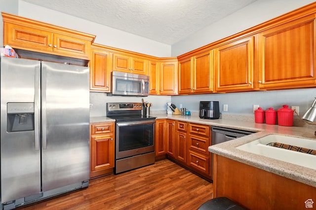 1587 N 565 W Unit 101, Logan, UT 84341 - kitchen with stainless steel appliances, dark wood finished floors, brown cabinetry, a textured ceiling, and a sink