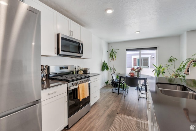 1073 E Dory Boat Rd, Saratoga Springs, UT 84045 - kitchen with appliances with stainless steel finishes, dark countertops, a sink, a textured ceiling, and wood finished floors