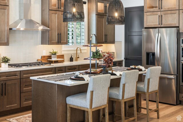 1252 W 770 S Unit 104, Heber City, UT 84032 - kitchen featuring appliances with stainless steel finishes, wall chimney range hood, glass insert cabinets, tasteful backsplash, and a kitchen breakfast bar