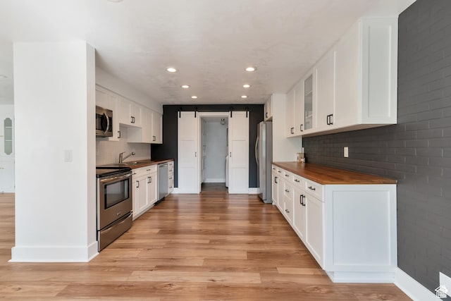 265 N Vine St W Unit 1, Salt Lake City, UT 84103 - kitchen featuring appliances with stainless steel finishes, a barn door, light wood finished floors, wood counters, and decorative backsplash