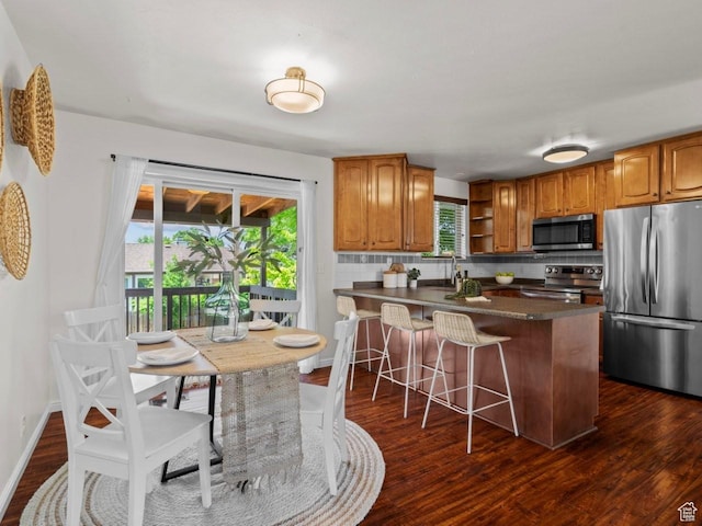 9750 S David St E, Sandy, UT 84070 - kitchen featuring appliances with stainless steel finishes, dark countertops, dark wood-style floors, a peninsula, and a breakfast bar area