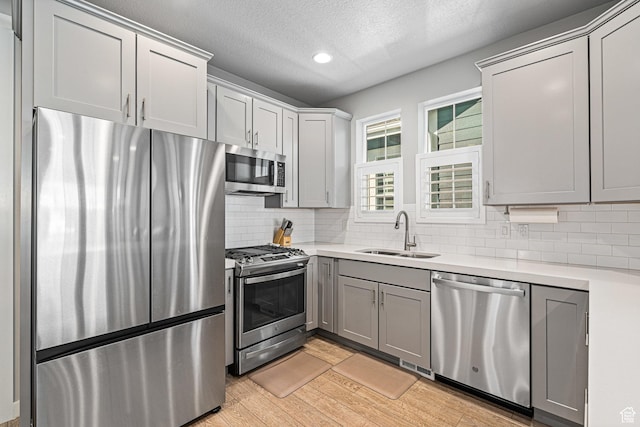 9857 N Featherstone Dr, Highland, UT 84003 - kitchen featuring appliances with stainless steel finishes, a sink, light countertops, light wood-style flooring, and backsplash