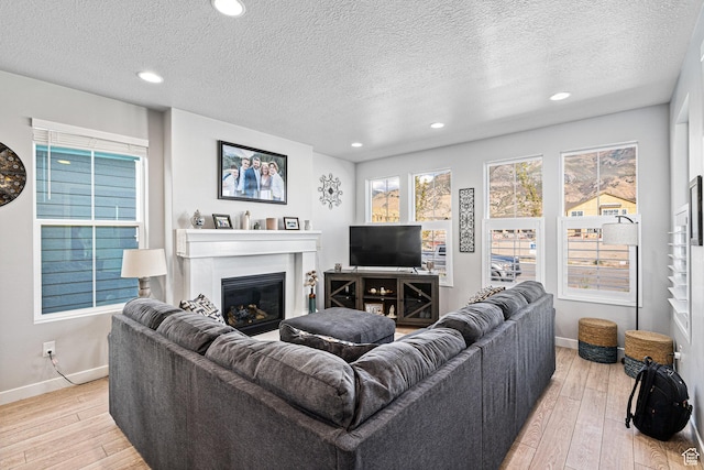 9857 N Featherstone Dr, Highland, UT 84003 - living area featuring a glass covered fireplace, baseboards, light wood-style flooring, a textured ceiling, and recessed lighting