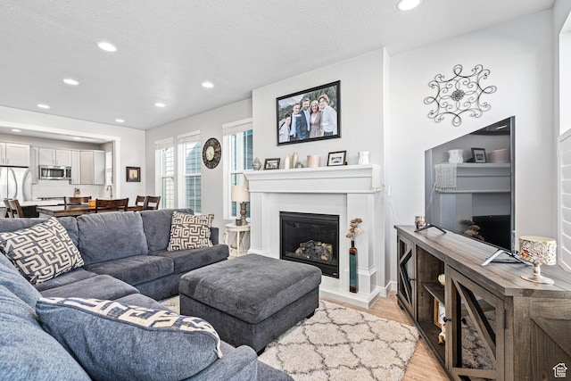 9857 N Featherstone Dr, Highland, UT 84003 - living room featuring recessed lighting, light wood-style flooring, a glass covered fireplace, and a textured ceiling
