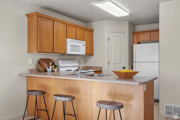 8064 N Clearwater Rd, Eagle Mountain, UT 84005 - kitchen with white appliances, a peninsula, a kitchen bar, baseboards, and light tile patterned flooring