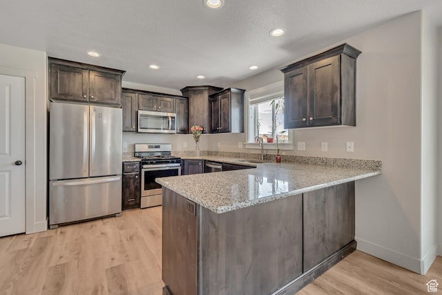 182 W Braeburn Ln, Santaquin, UT 84655 - kitchen with stainless steel appliances, a peninsula, dark brown cabinetry, light wood-style floors, and light stone countertops