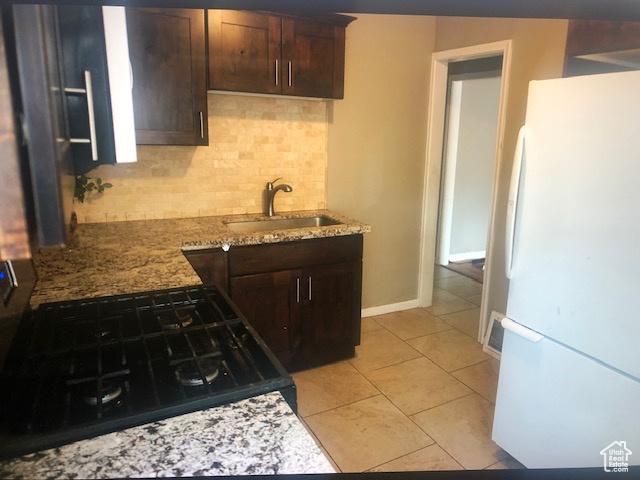 2726 S Cyprus Ln, Magna, UT 84044 - kitchen featuring freestanding refrigerator, a sink, tasteful backsplash, dark brown cabinetry, and light stone countertops