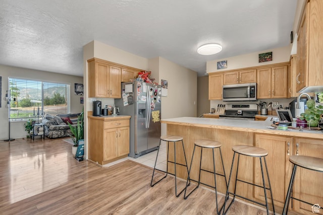 2316 E Claybourne Ave S, Millcreek, UT 84109 - kitchen with appliances with stainless steel finishes, a peninsula, light countertops, light wood finished floors, and a kitchen breakfast bar
